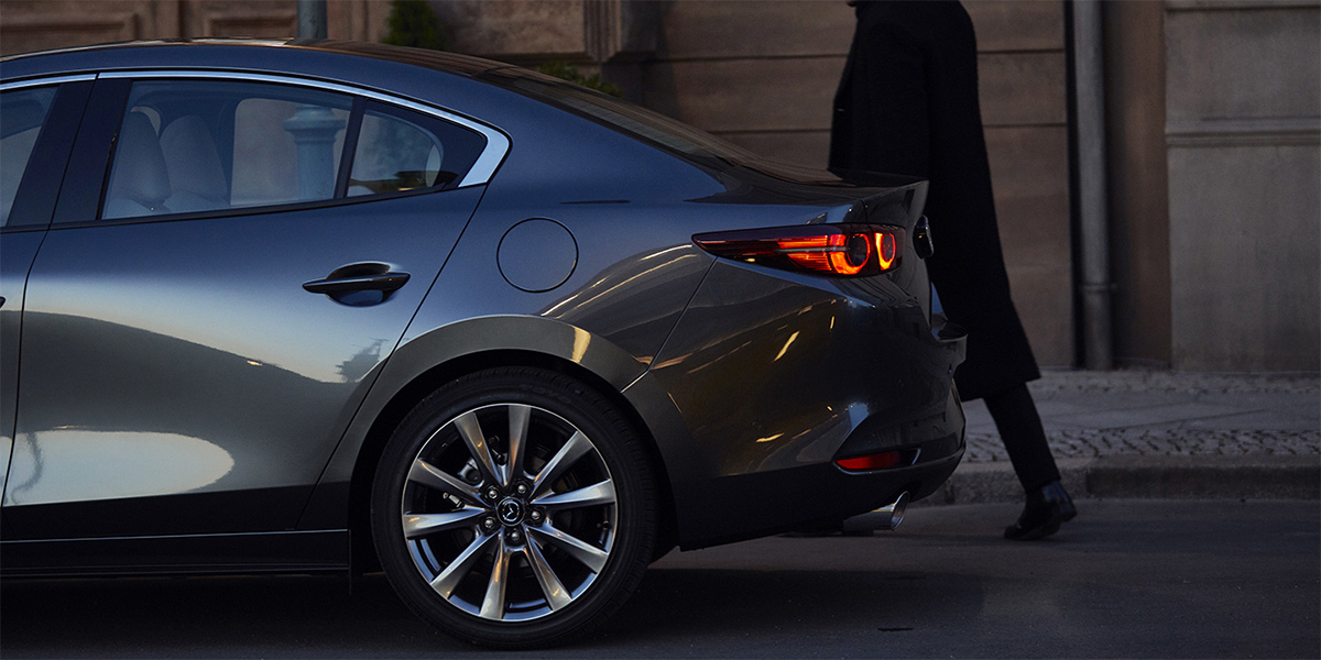 Person walking to the back of a Gray 2019 Mazda3 Sedan