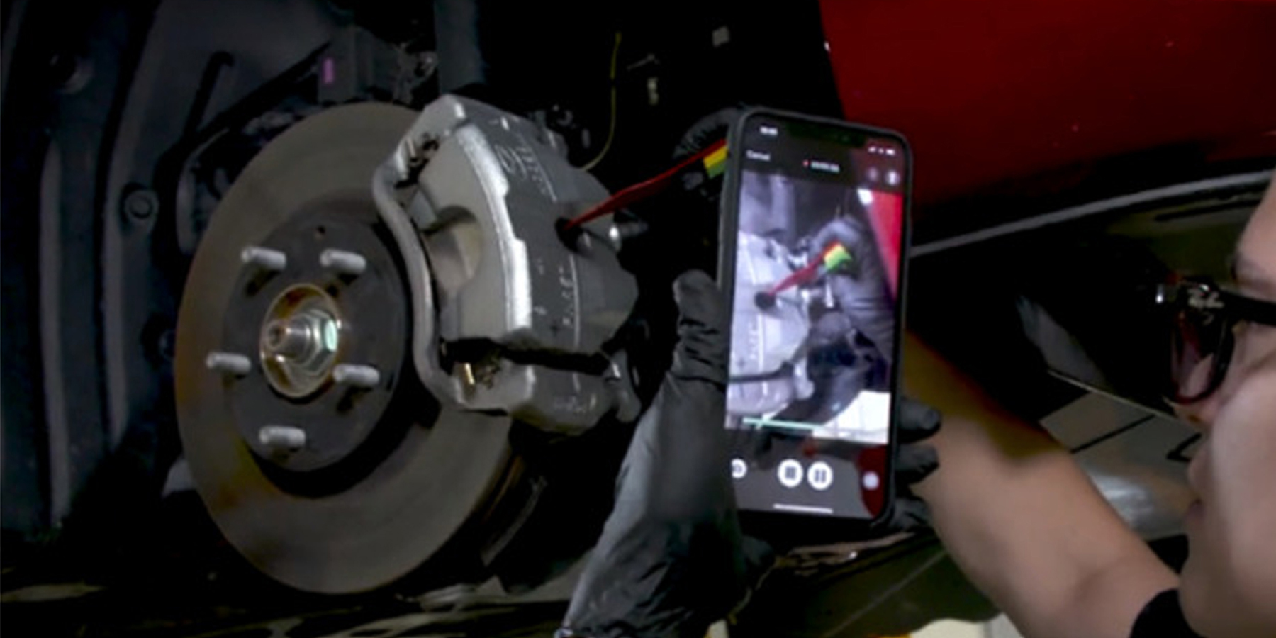 A man fixing his vehicle by following a video on his smart phone
