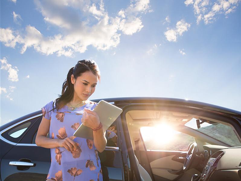 Woman standing by her car looking at a tablet.
