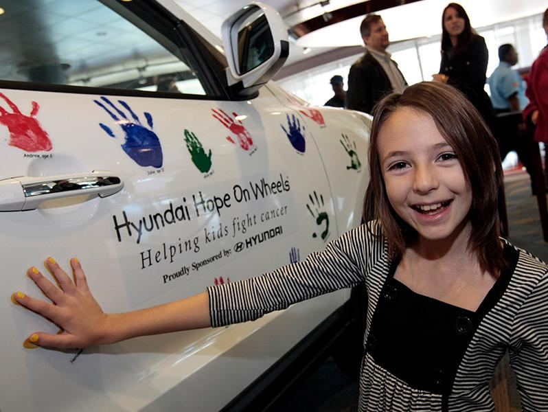 Girl with hand on Hyundai Hope On Wheel vehicle.