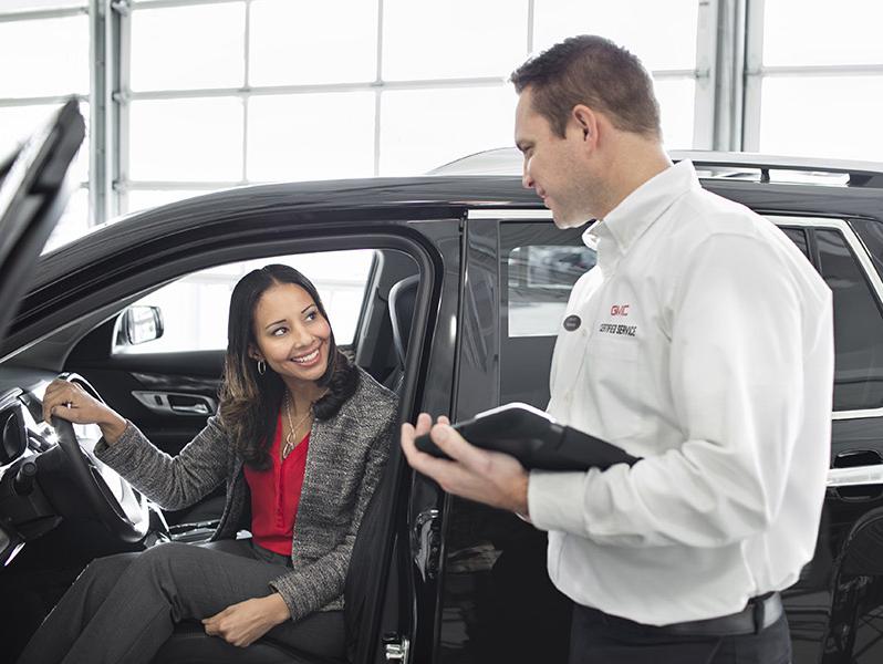A GMC salesman helping a woman who is shopping for a new car.