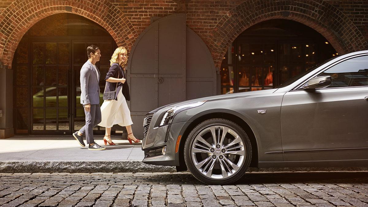 A couple walking in front next to a Cadillac CT6.