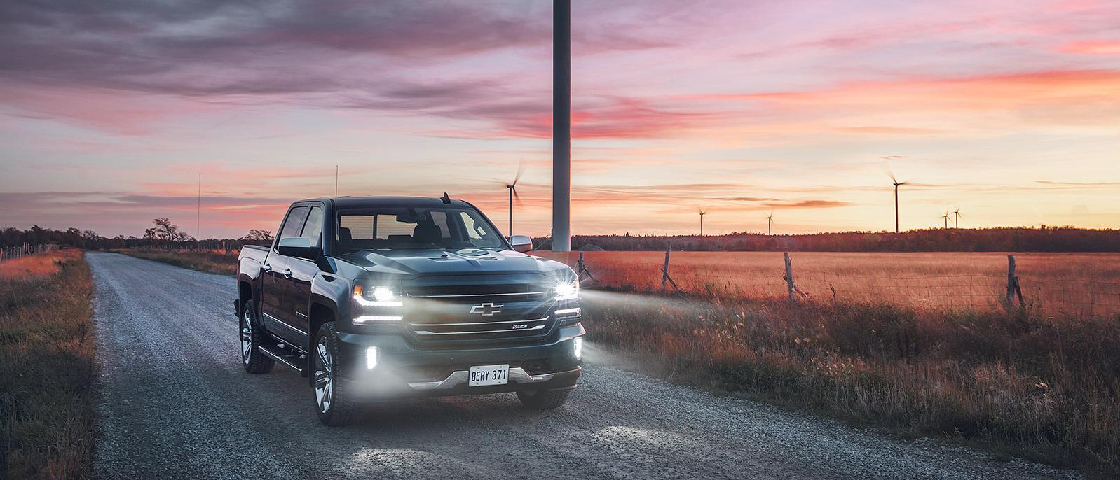 A 2018 Chevy Silverado 1500 driving down a country road at sunset.