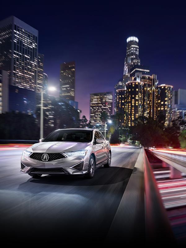 A silver Acura ILX driving in a city at night.