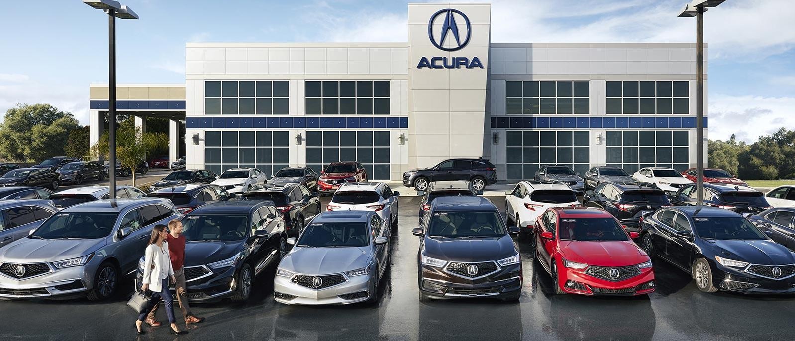 A couple walking along a row of new Acura vehicles at the dealership.