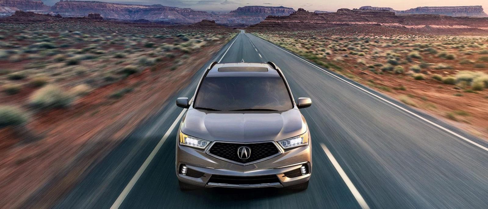 A silver Acura MDX driving on a desert highway at dusk.