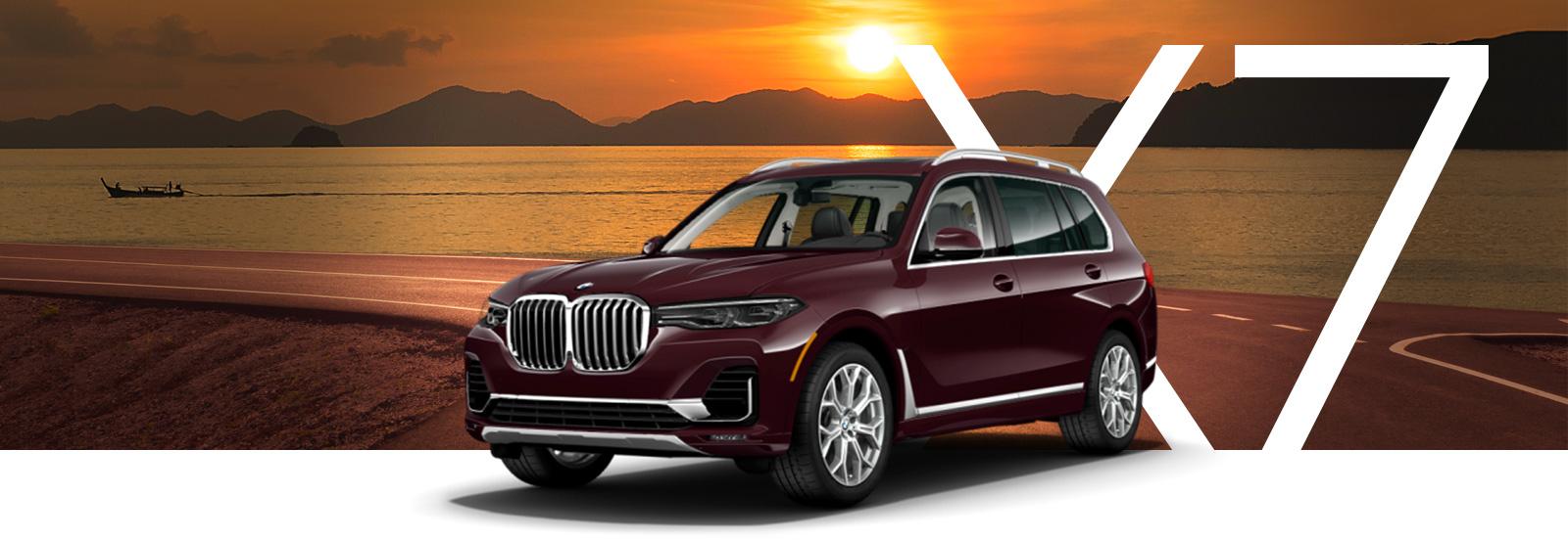 A burgundy BMW X7 parked on a bay-side road at sunset.