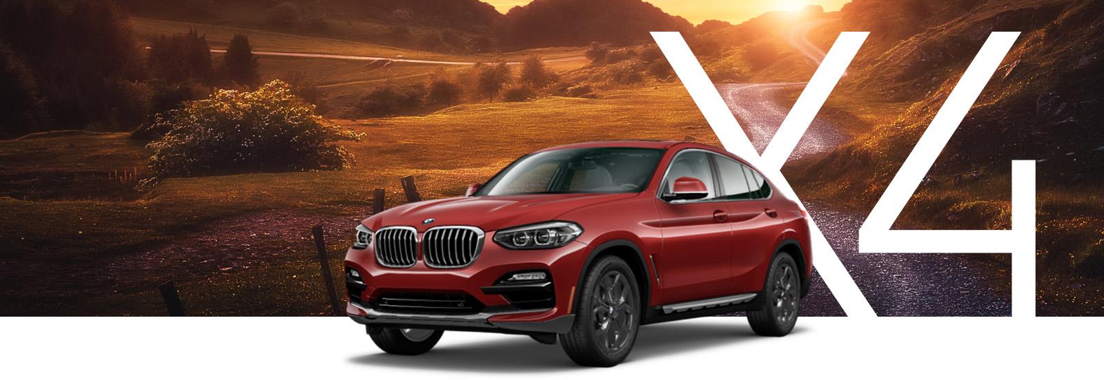 A red BMW X4 driving along a winding desert road at sunset.