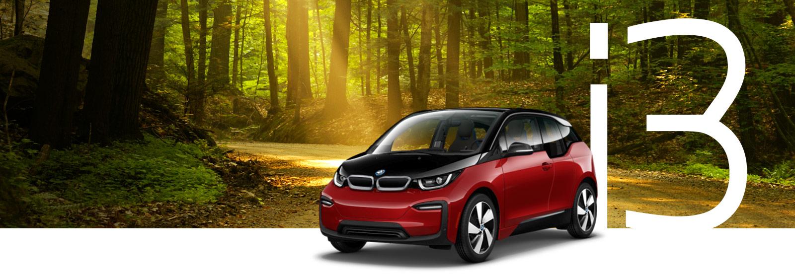 A red BMW i3 in a sunlit forest.