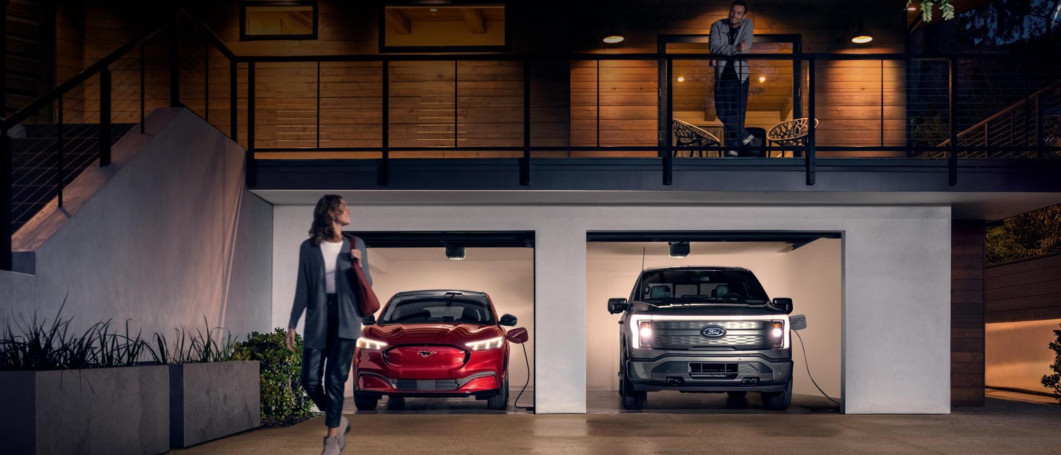 Woman walking out from home garage with a 2024 Mustang® Mach-E and Ford Lightning® truck in plugged-in and charging