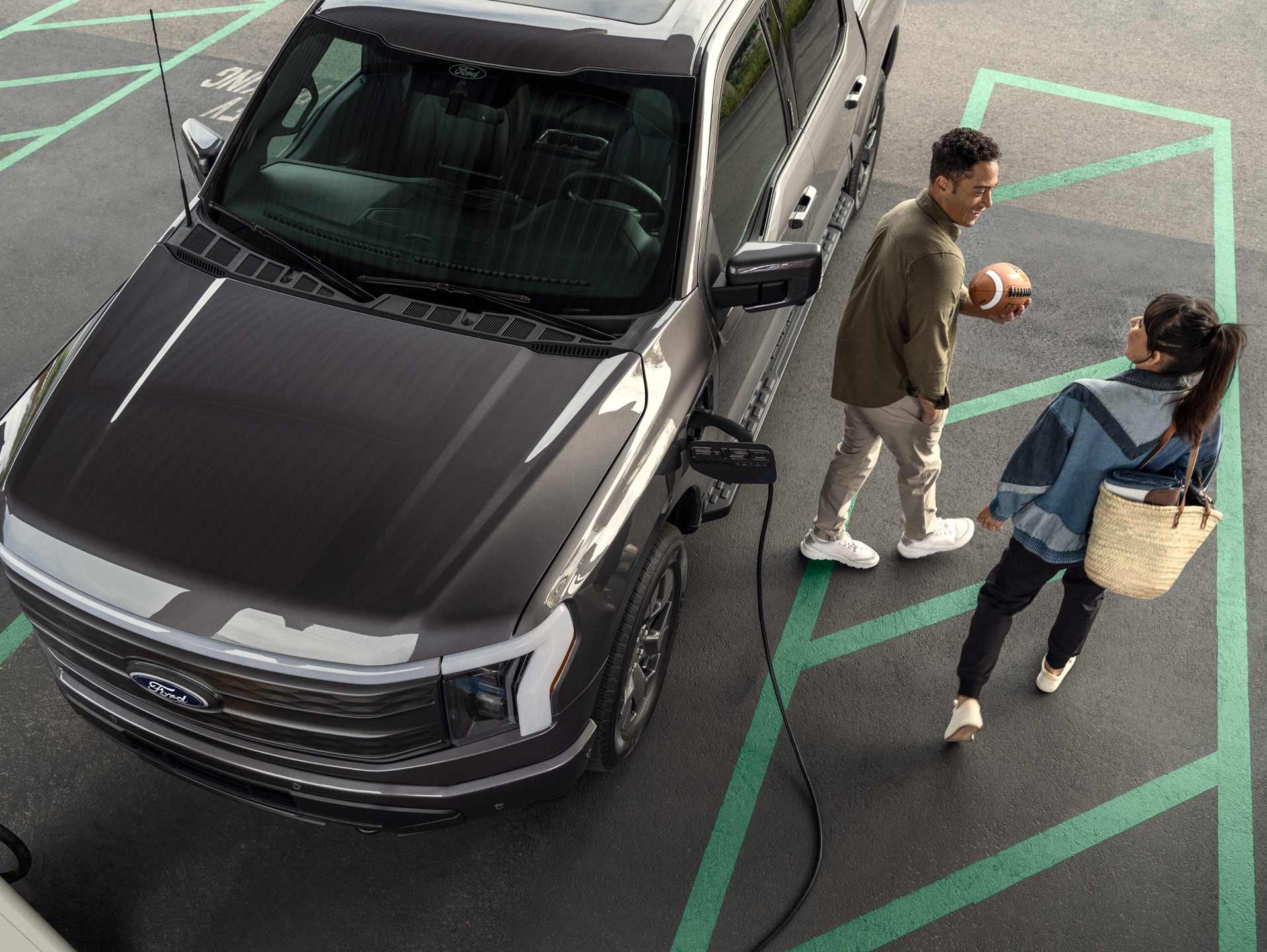 Overhead shot of a couple walking away from a 2024 Ford Lightning® that is plugged in and charging