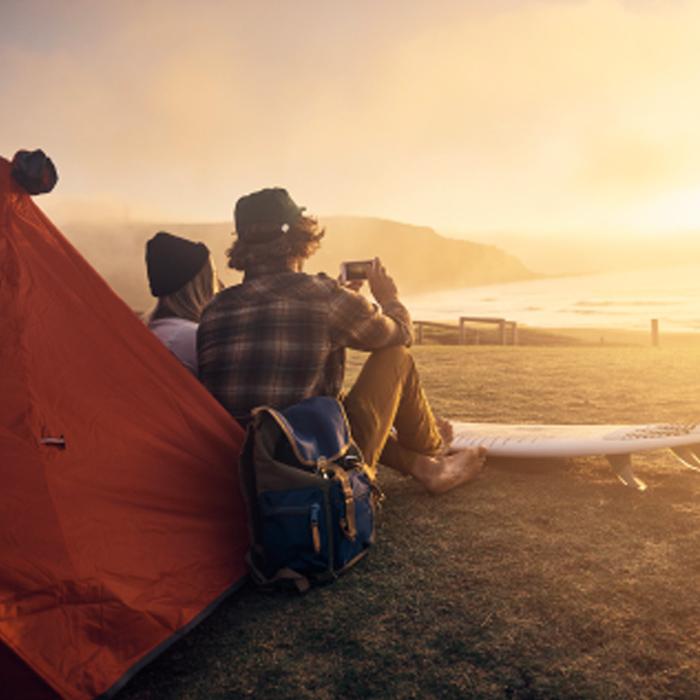 Two people sitting on the beach next to a tent taking pictures of the sunrise. 