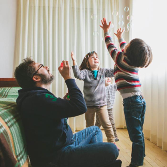 A man and two children catching bubbles indoors. 
