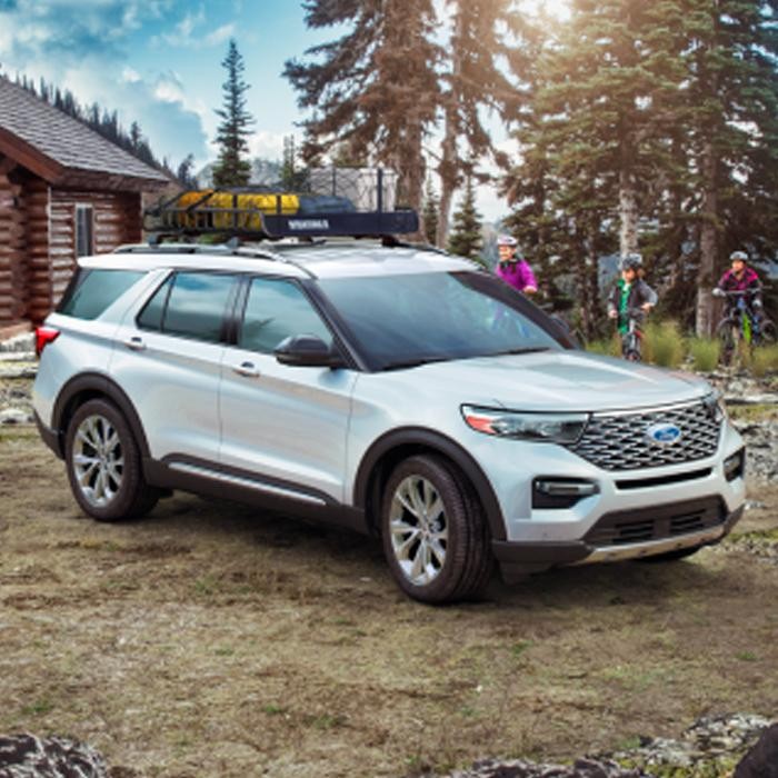 A white explorer parked at a campsite next to three people riding bicycles. 