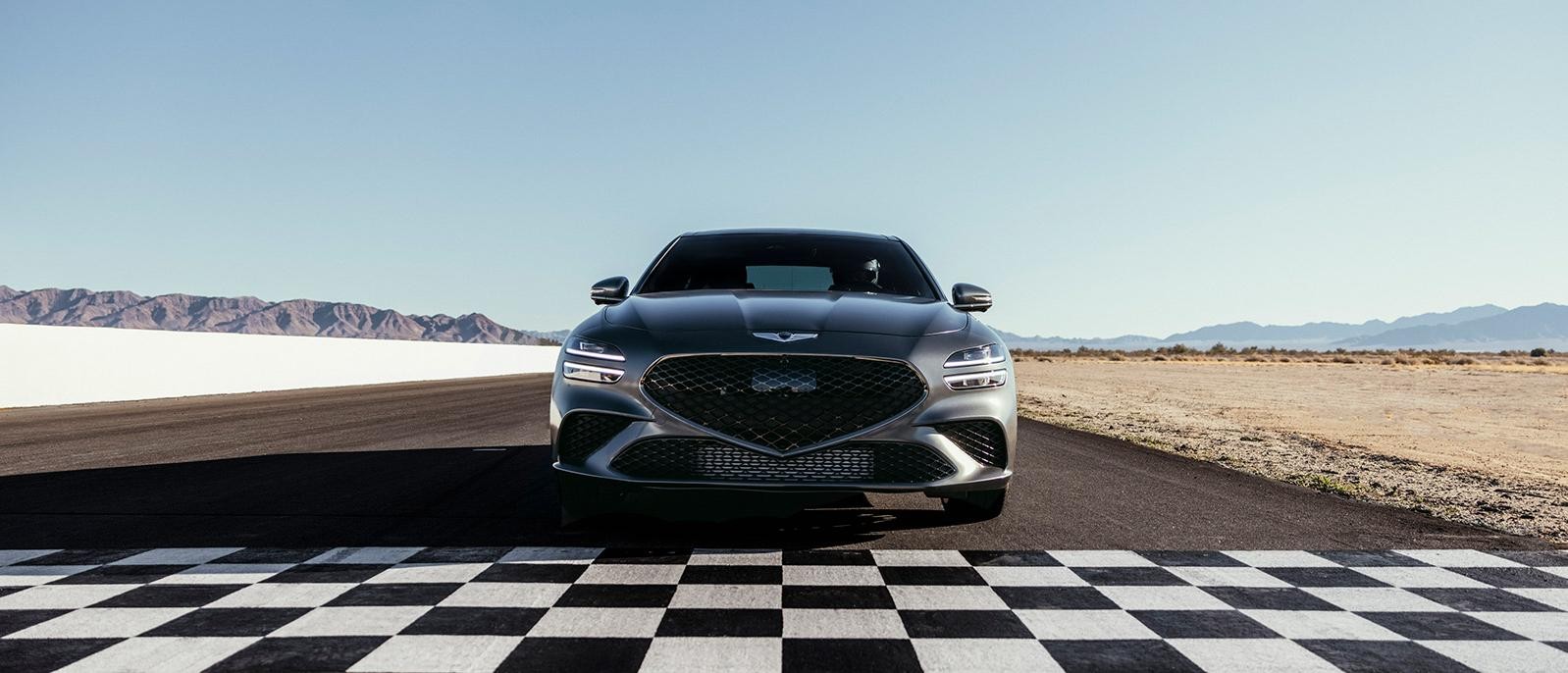 Head-on view of a Silver Genesis G70 at the checkered finish line of a desert racetrack.