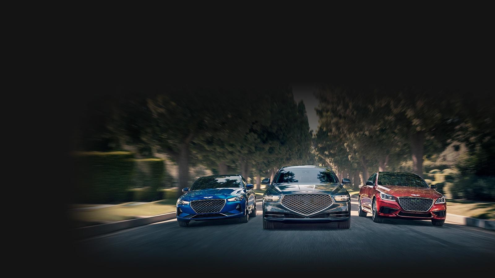 Head on view of three Genesis pre-owned vehicles coming down a tree-lined suburban street.