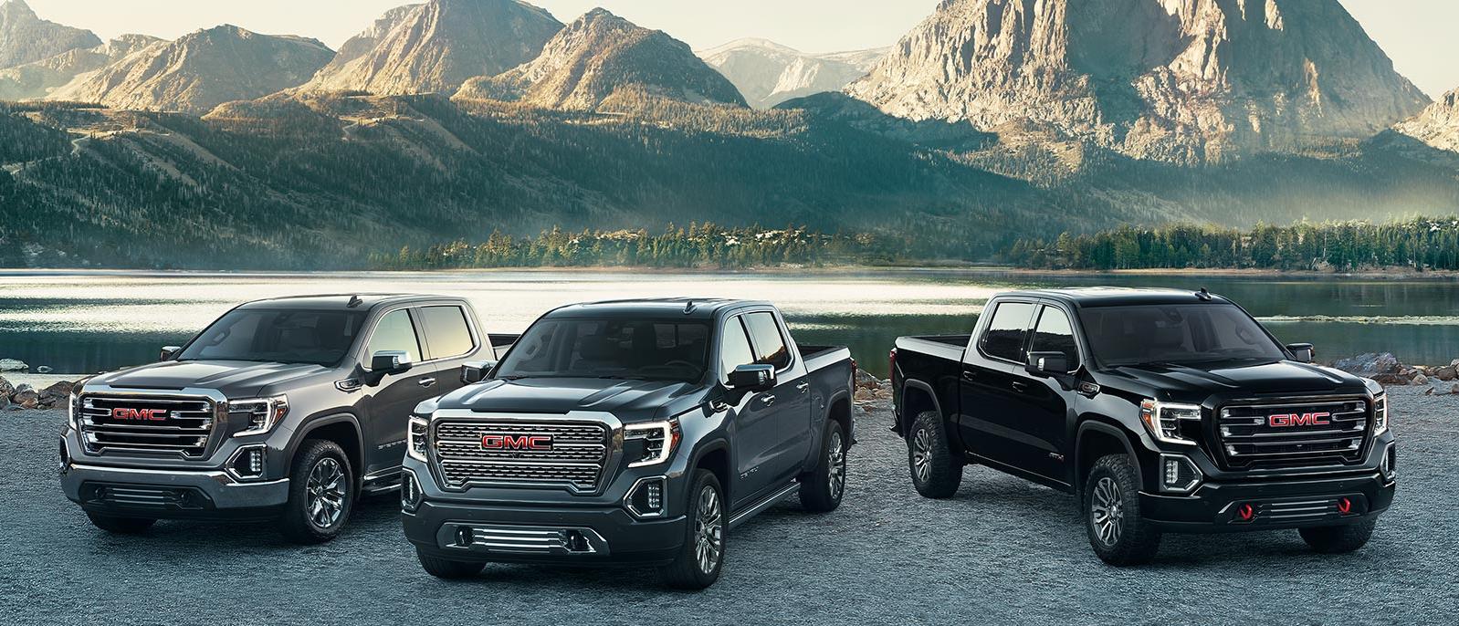 A lineup of GMC Sierra 1500 trucks parked in front of a mountain lake.