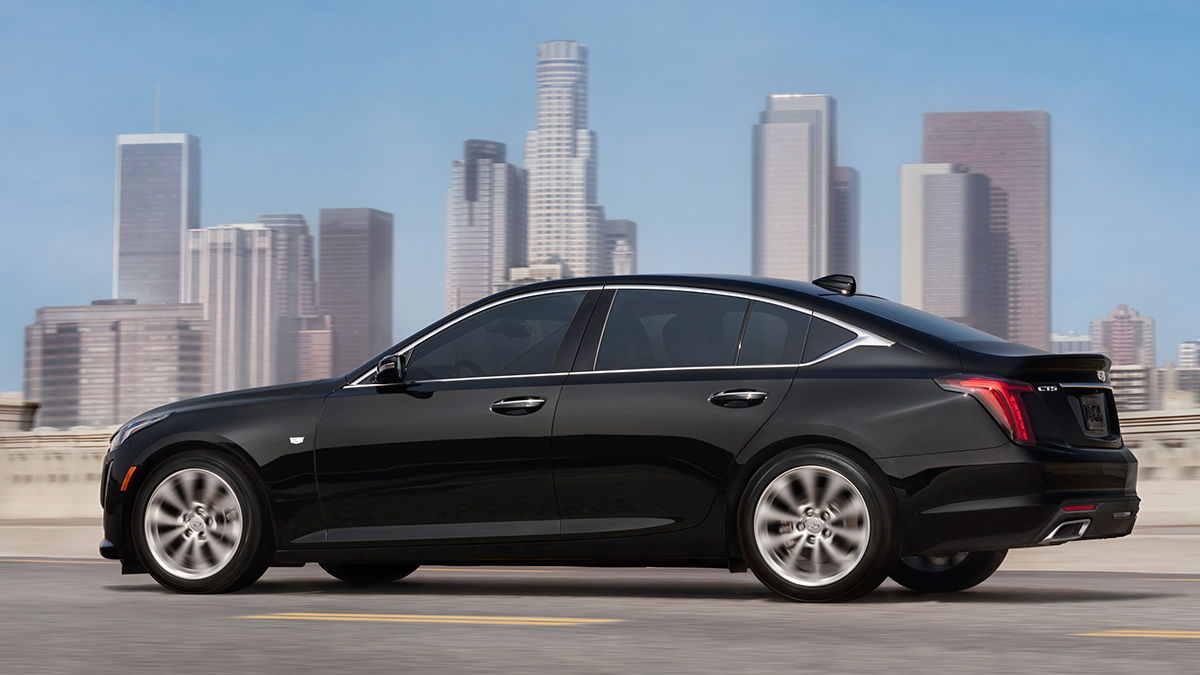 A profile view of a black Cadillac CT5 driving in front of a city.