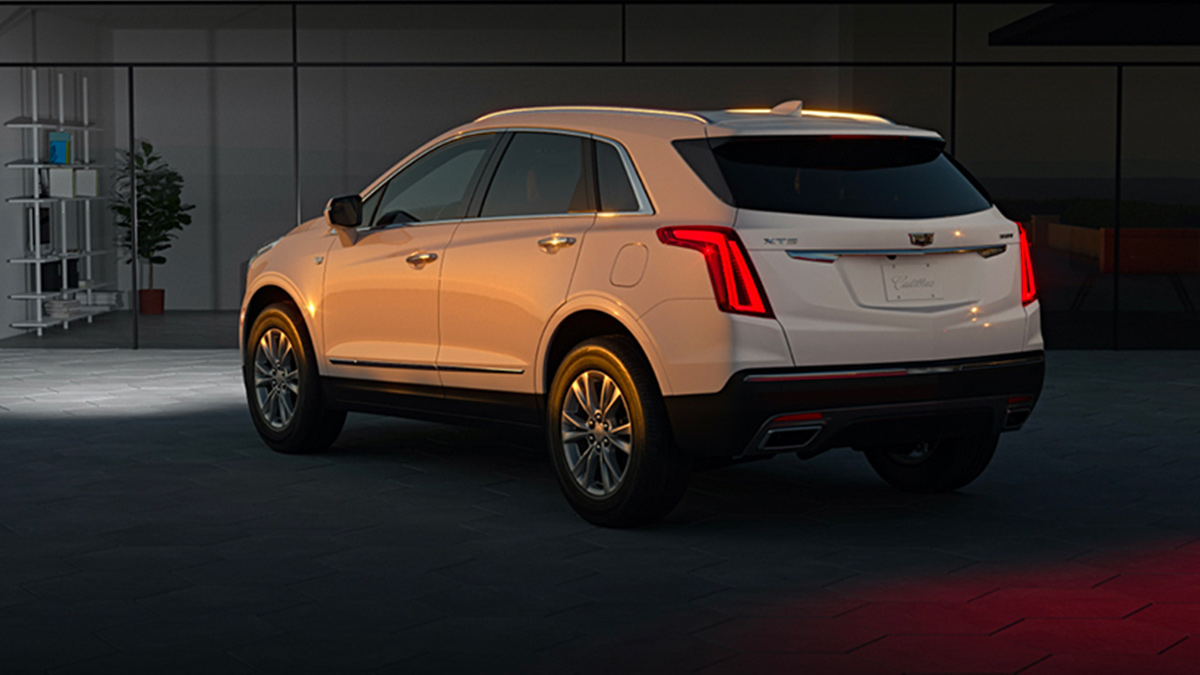 A white Cadillac XT5 parked in a driveway at dusk with the taillights glowing.