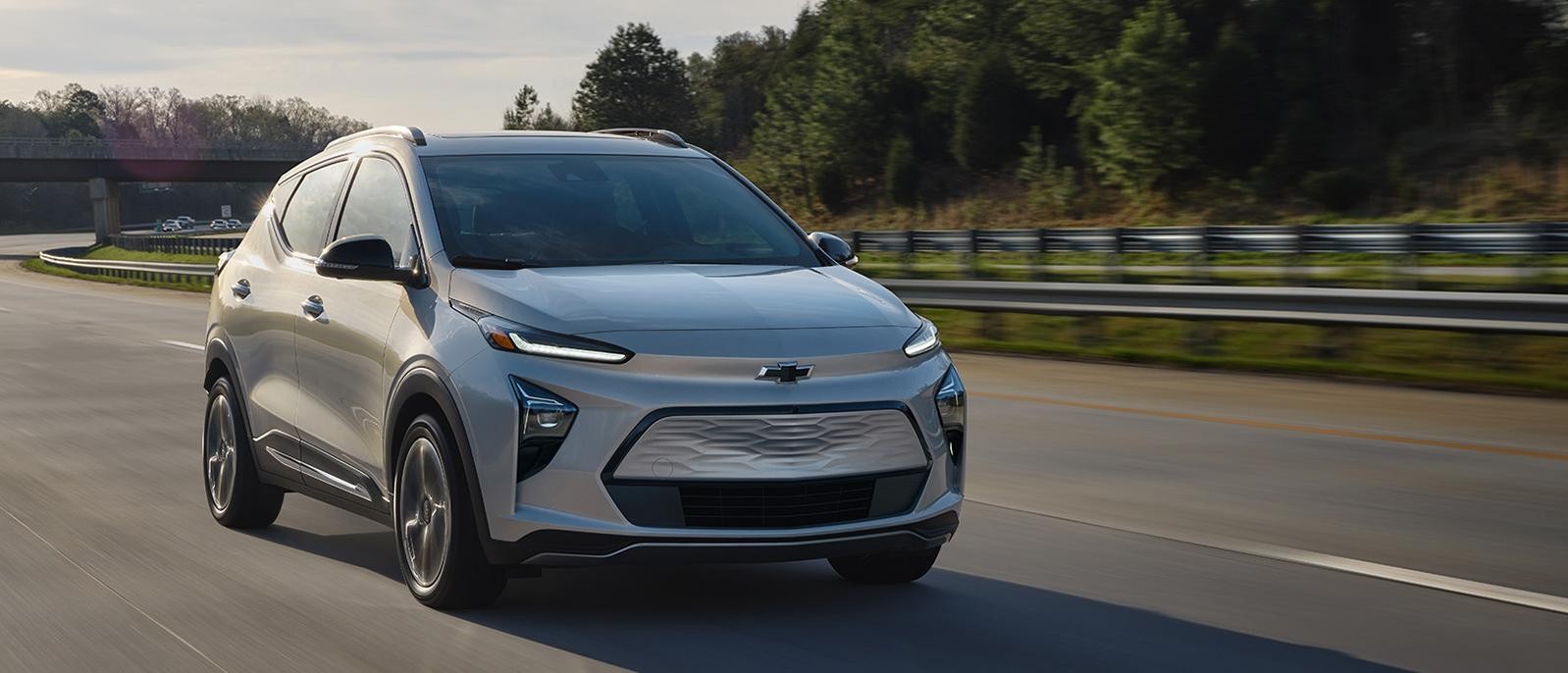 A light blue Chevy Bolt EUV driving on a countryside highway.