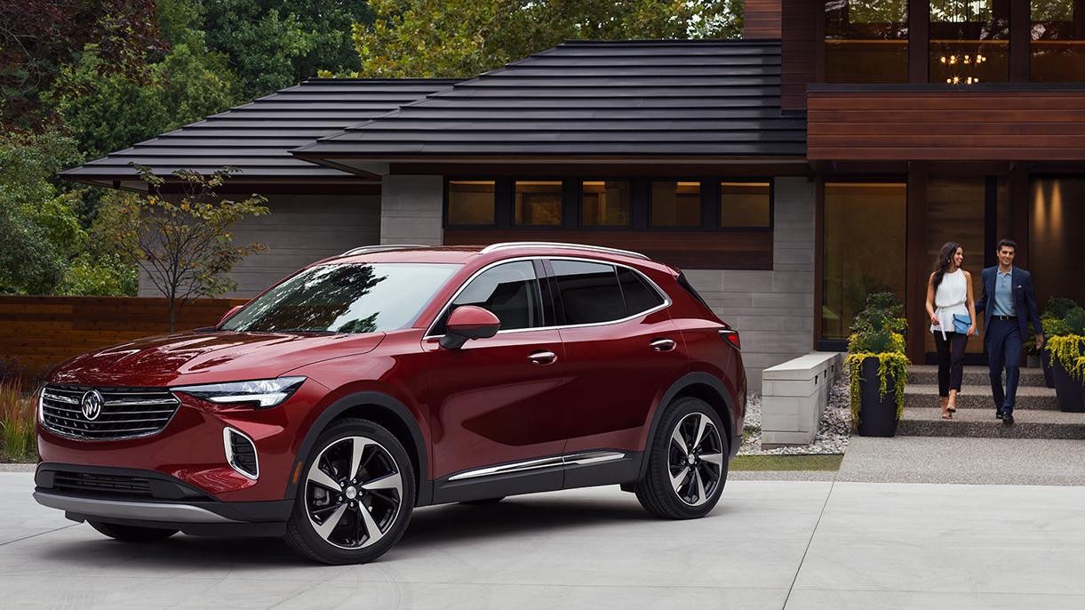 A red Buick Envision parked in the driveway of a modern home with a couple approaching.