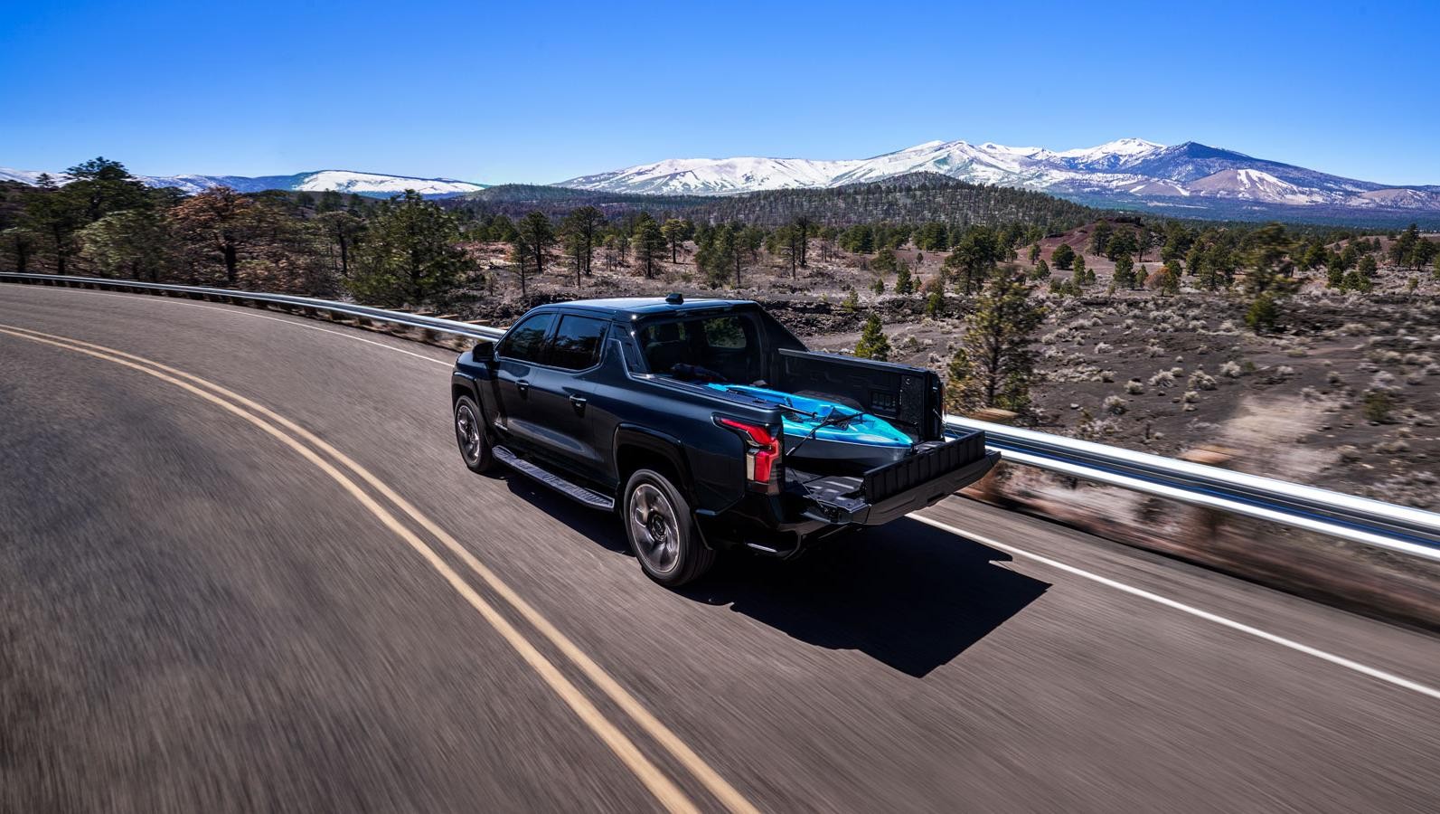 Black 2024 Chevrolet Silverado EV driving with a kayak in the bed