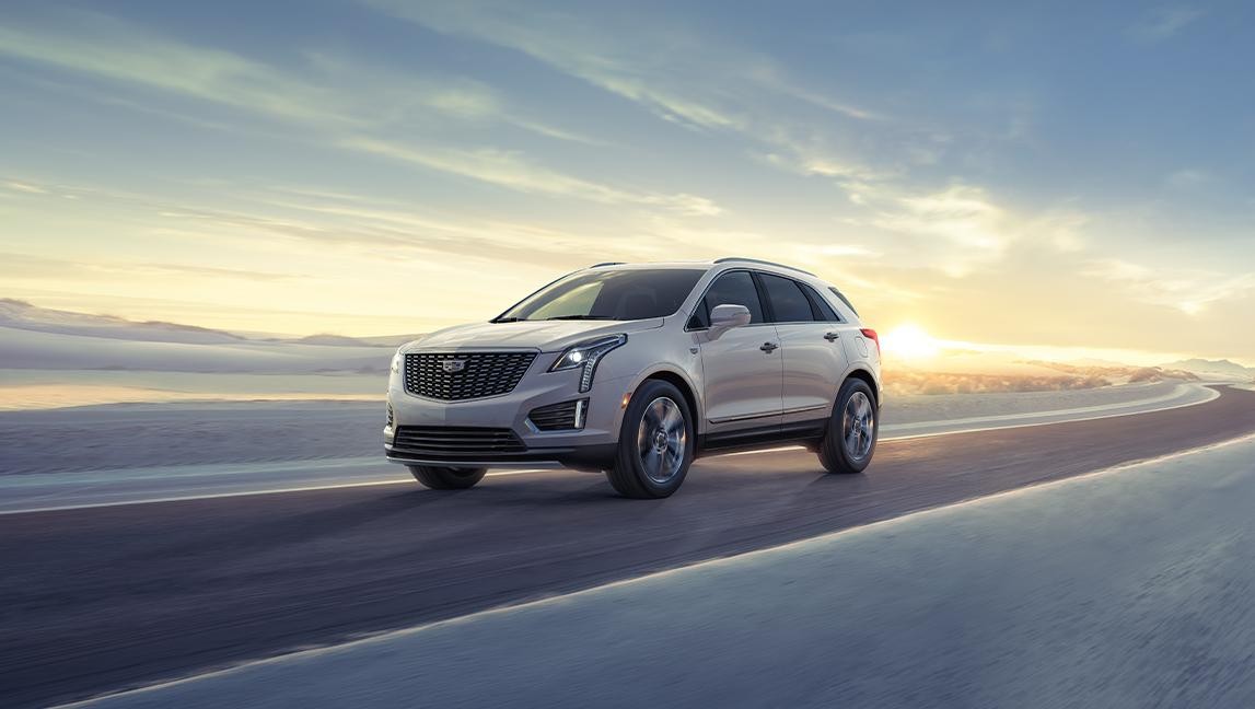 The 2024 Cadillac XT5 Driving on a Winding Road with Sun Rising in Background