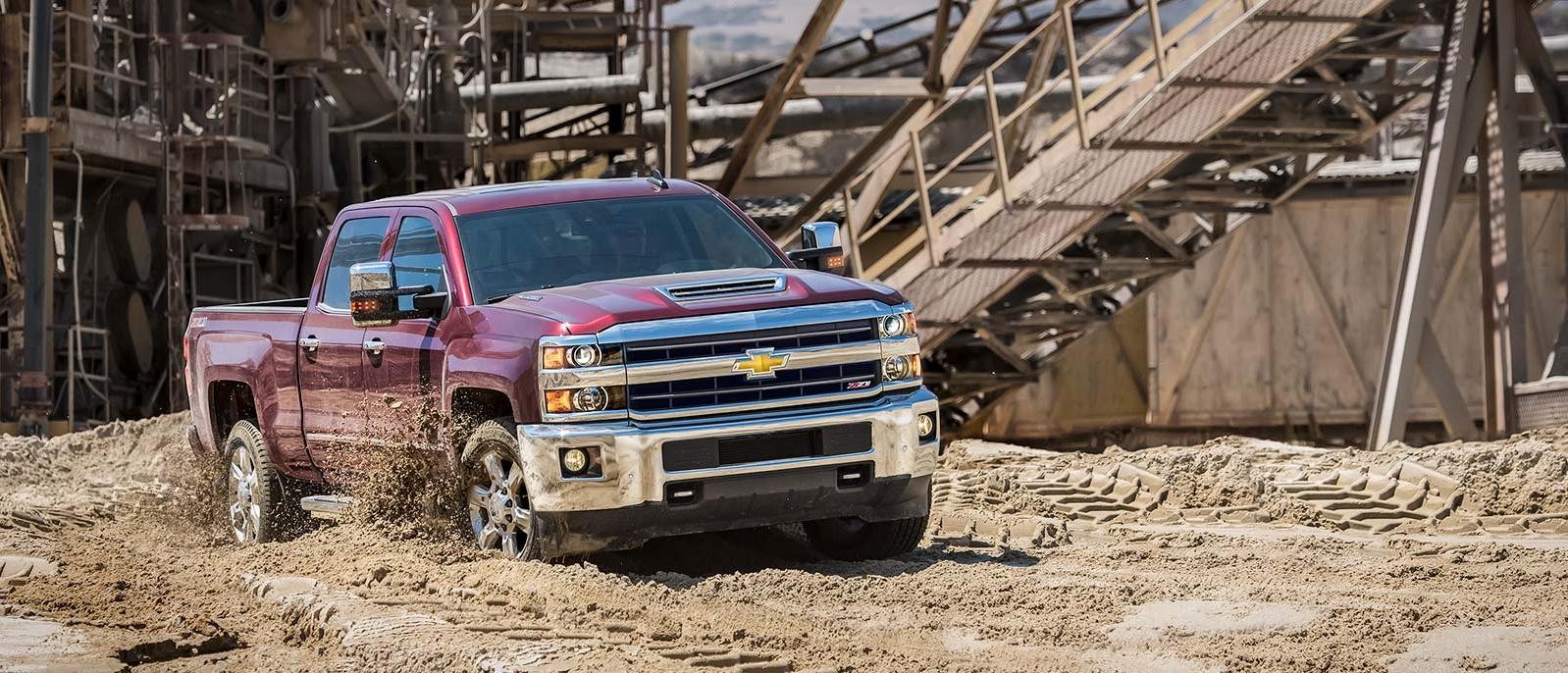 A red Chevrolet Silverado 2500HD Crew Cab driving through a muddy work site.