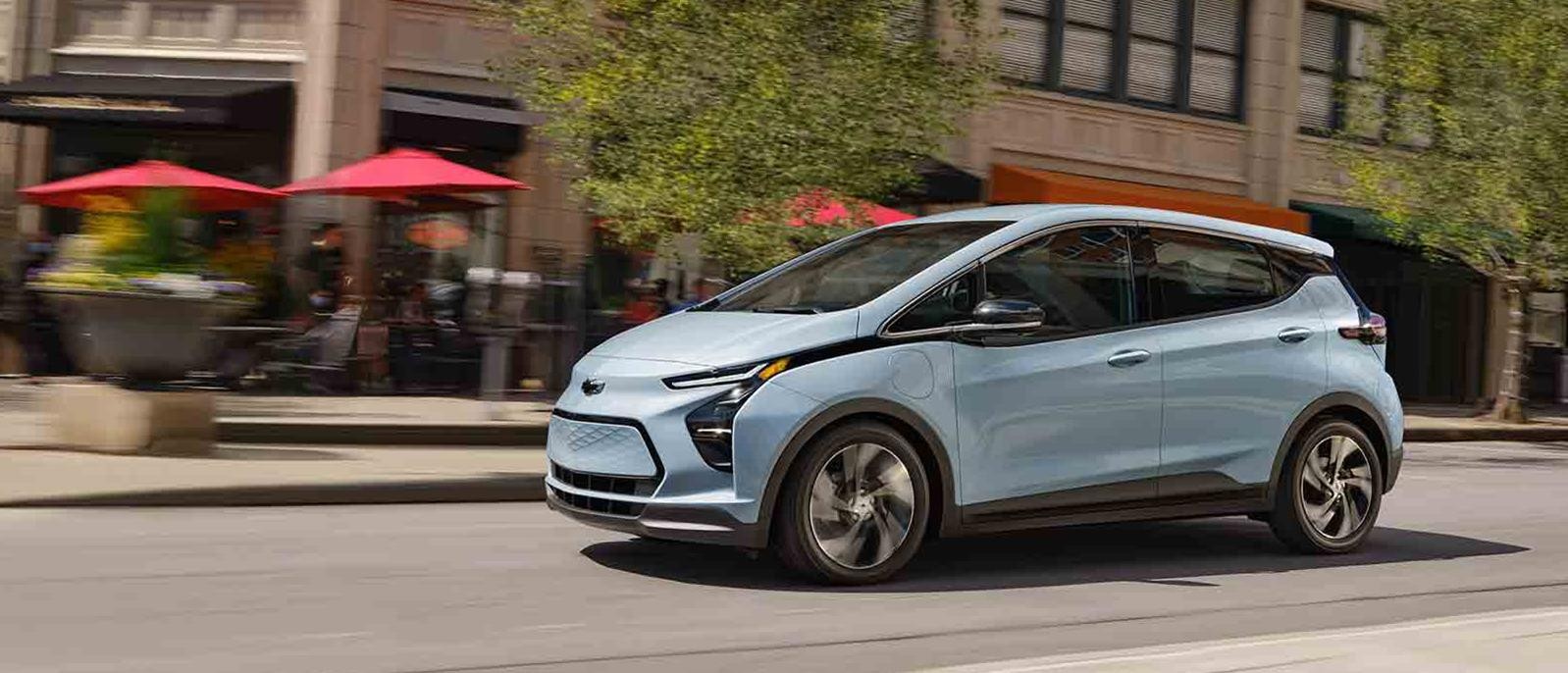 A light blue Chevy Bolt EV driving down a city street.