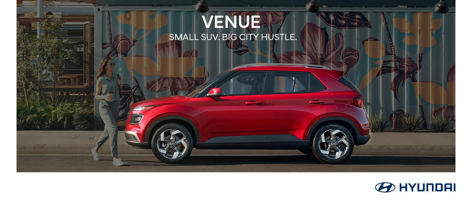 Red 2023 Hyundai Venue parked with graffiti in background.