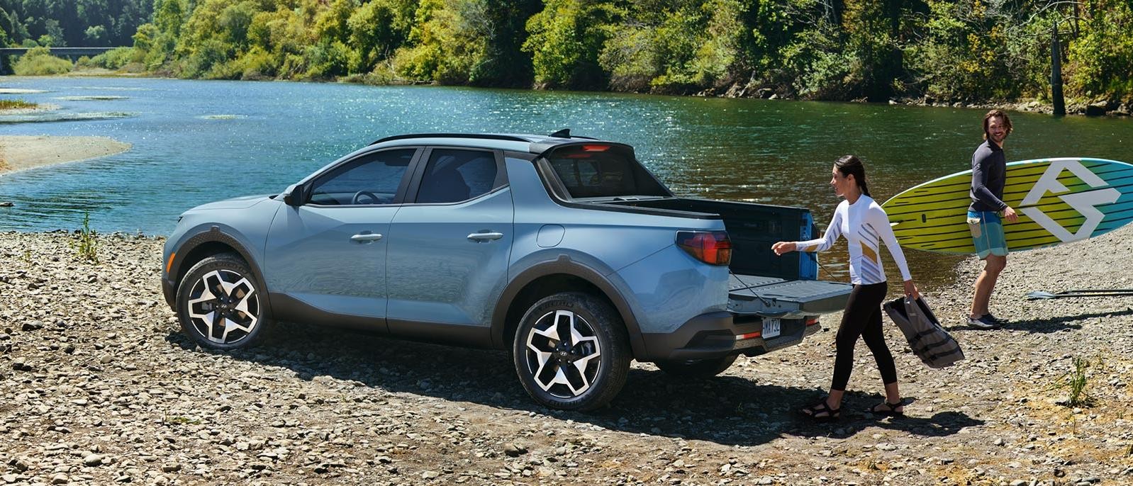 A couple unloading paddle boards and gear from their Hyundai Santa Cruz next to a river.