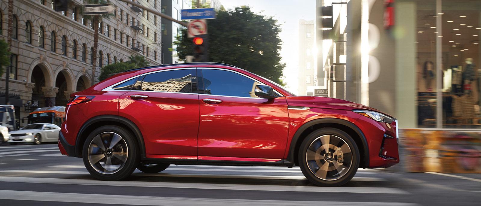 Profile view of a red INFINITI QX55 driving through a city.