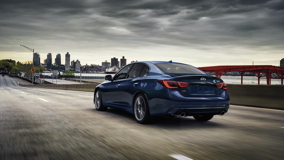 Blue INFINITI Q50 driving on a road going by a bridge