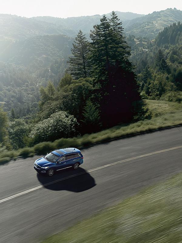 A high-angle view of a blue INFINITI QX60 driving along a curvy mountain road.