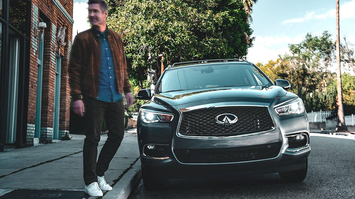 A man stepping into the street in front of a parked INFINITI QX60.