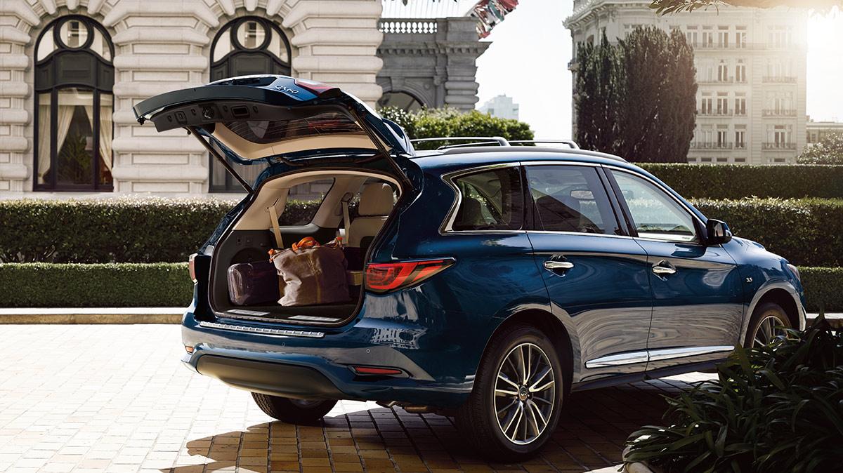 A blue INFINITI QX60 parked outside a hotel with the rear hatch open.