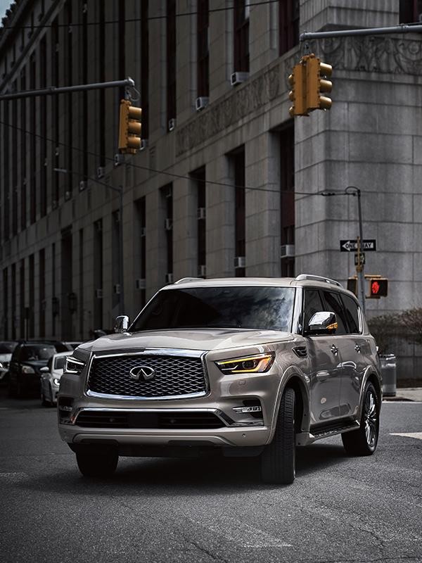 A tan INFINITI QX80 driving around a city street corner.