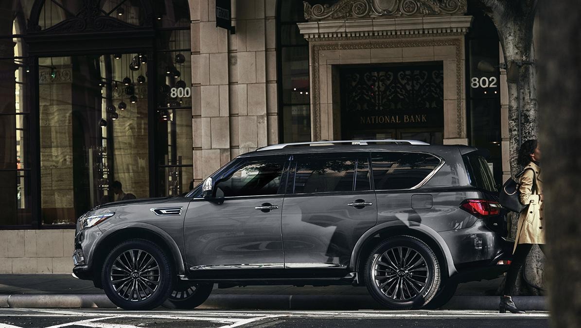 Profile view of a grey INFINITI QX80 parked in front of an old city bank.