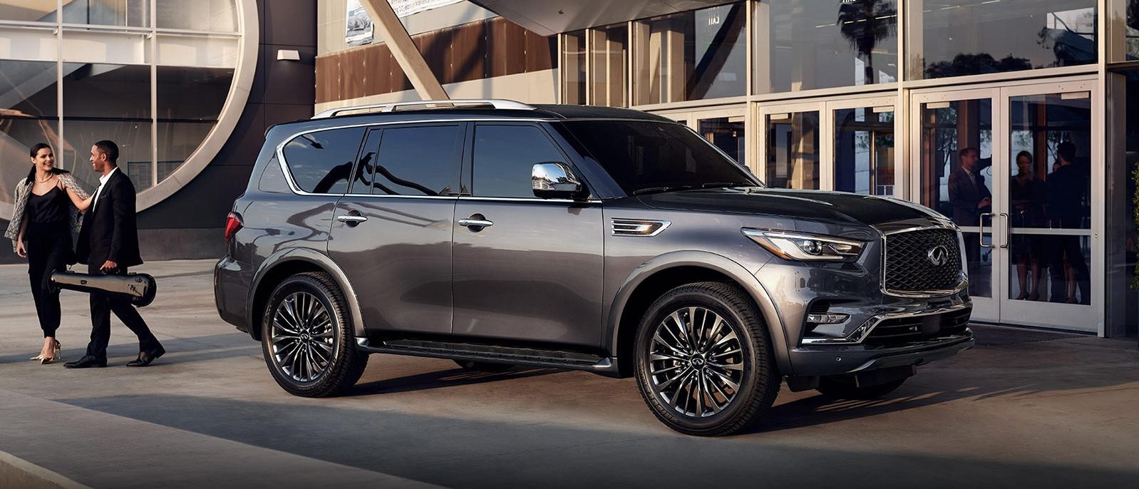 A couple walks behind a grey INFINITI QX80 parked in front of a concert hall.