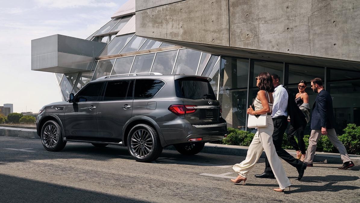 A grey INFINITI QX80 parked in front of a concert hall with people approaching.