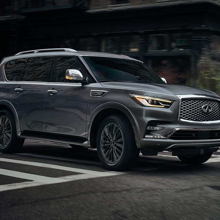 Side view of an INFINITI QX80 driving around a city corner.