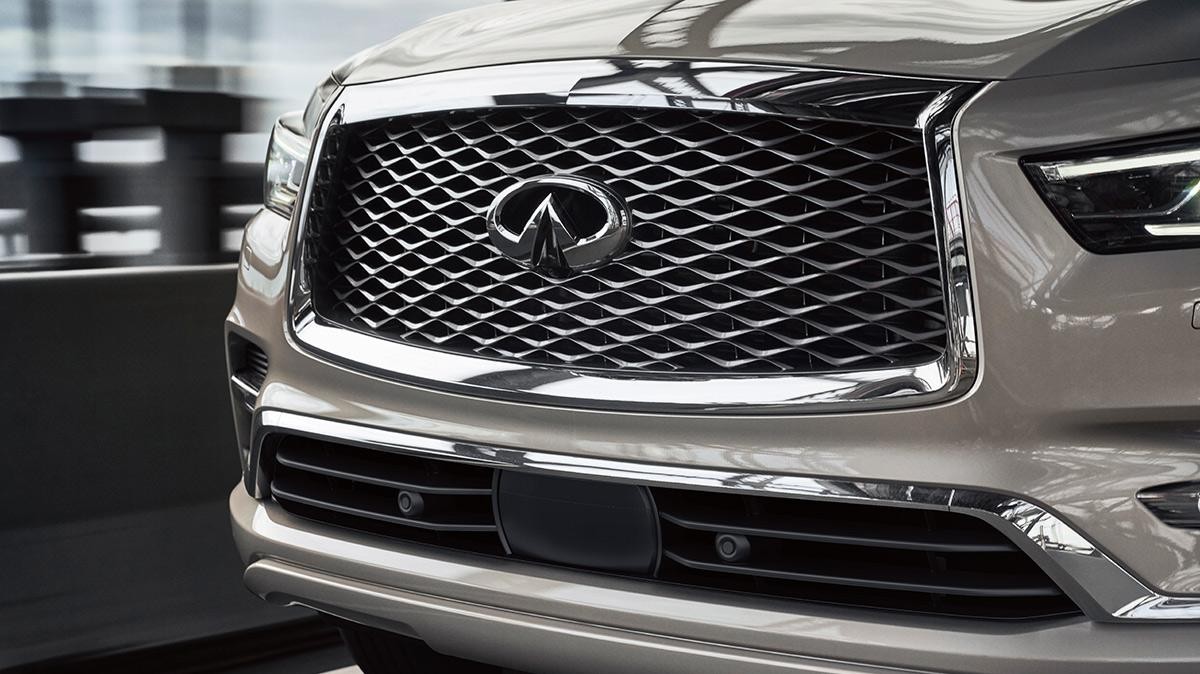 Close-up view of a tan INFINITI QX80 grille on a city street.