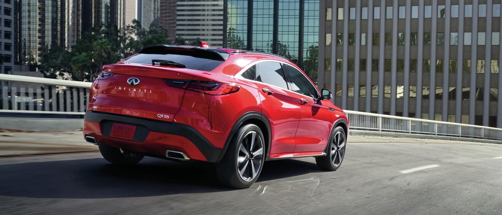 A red INFINITI QX55 driving along a city street.