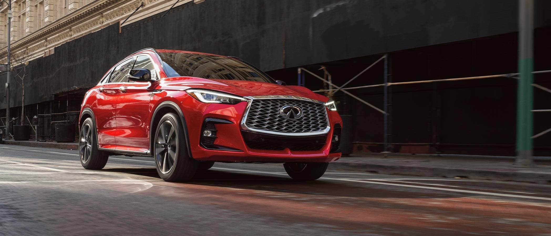 A red INFINITI QX55 driving along a city street.