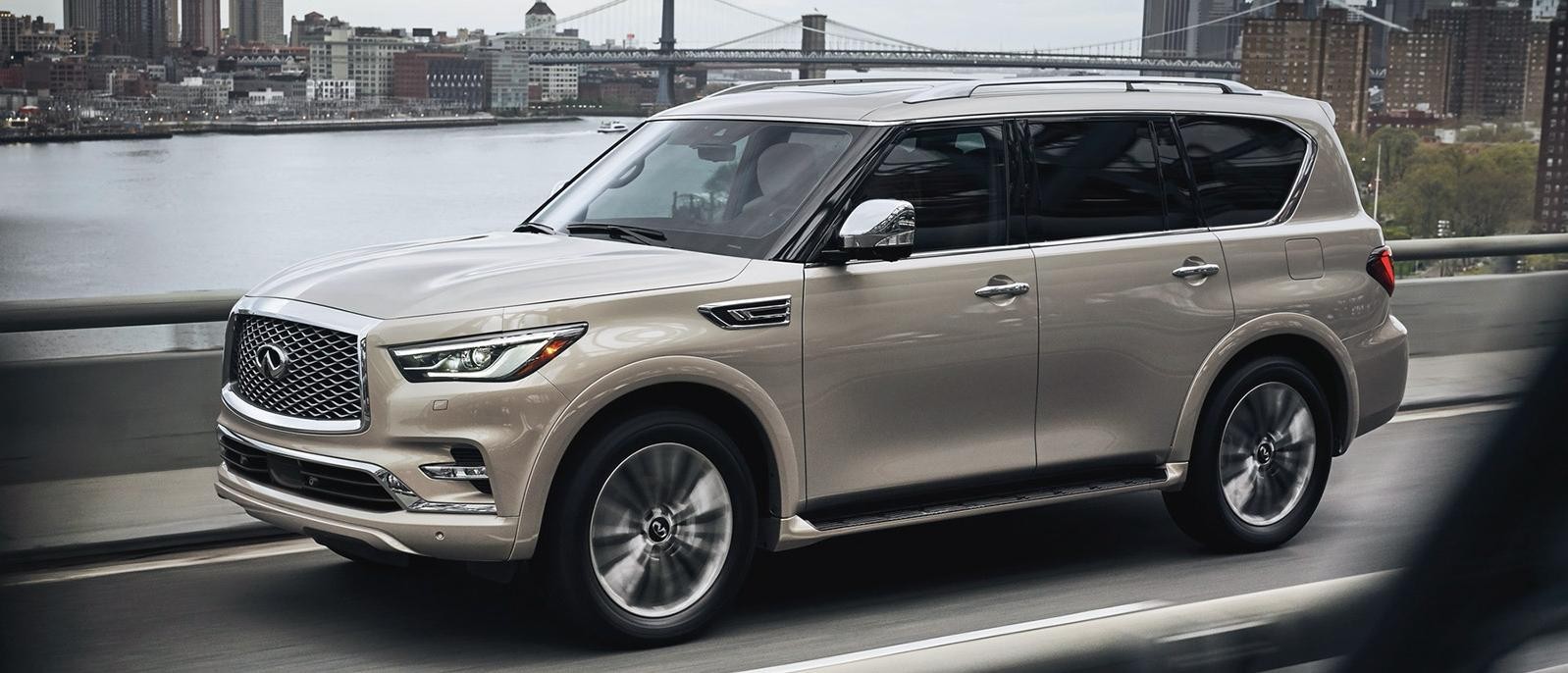 A silver INFINITI QX80 driving on a city bridge.