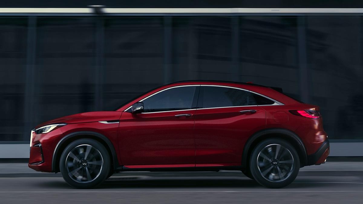 Profile view of a red INFINITI QX55 driving through a city street.