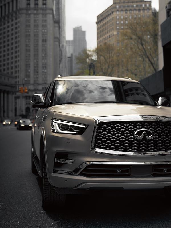 Nearly head-on view of a tan INFINITI QX80 driving through a city street.