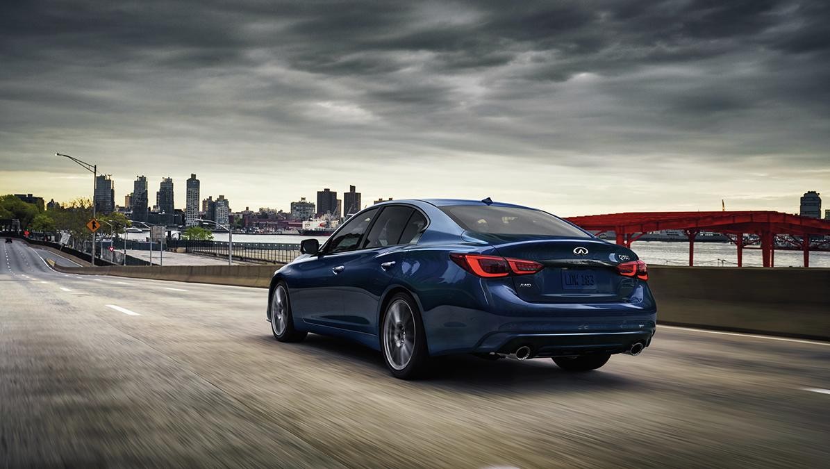 Blue INFINITI Q50 driving on a road going by a bridge