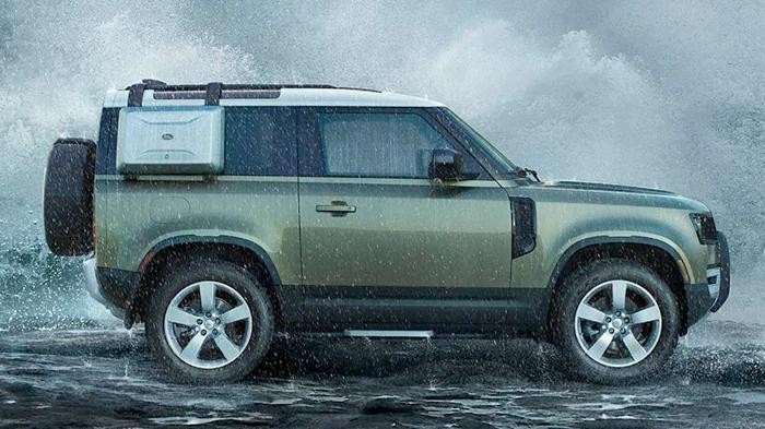 Profile of a green Land Rover Defender in front of breaking surf.