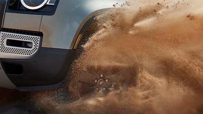 Close-up of a Land Rover Defender's tire kicking-up sand.